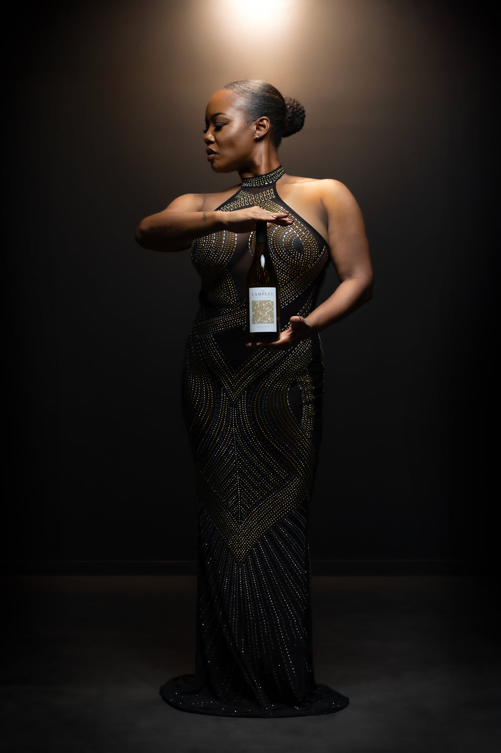 Chrishon Lampley in a beaded gown under a spotlight, holding The Lampley Chardonnay